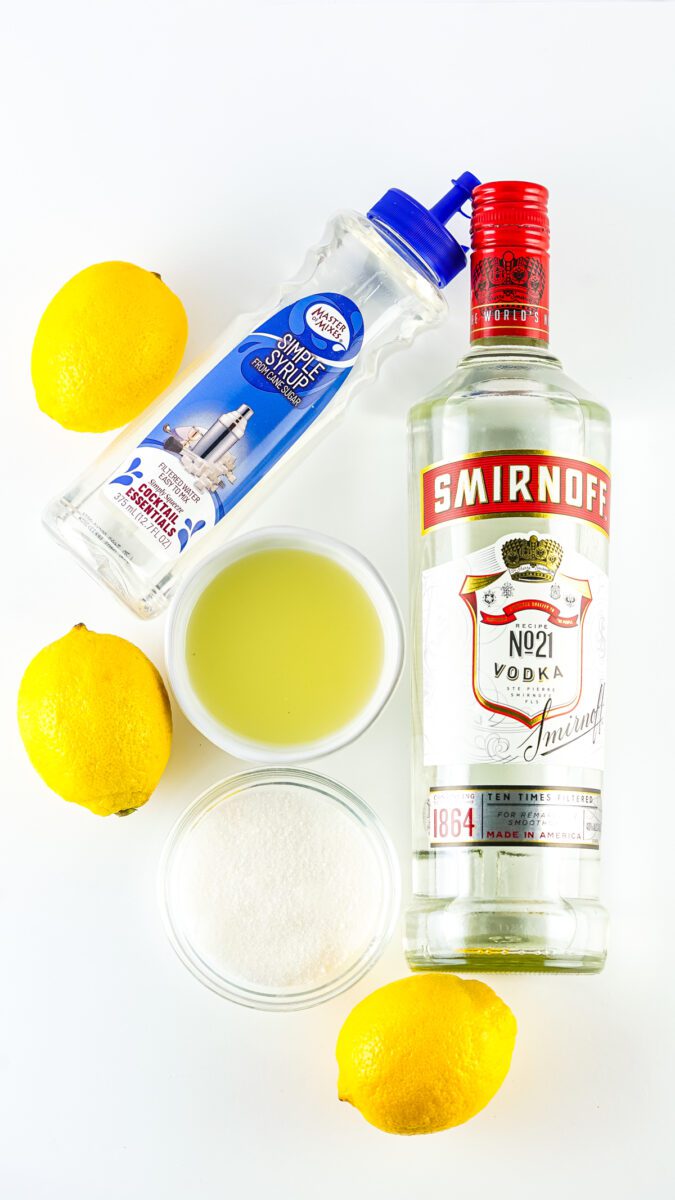 picture of the ingredients used in a Lemon Drop shot. Vodka bottle, Simple Syrup bottle, lemons and lemon juice