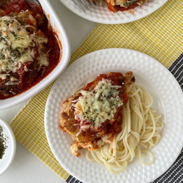 Chicken Cutlet Parmesan served with spaghetti on white plate.