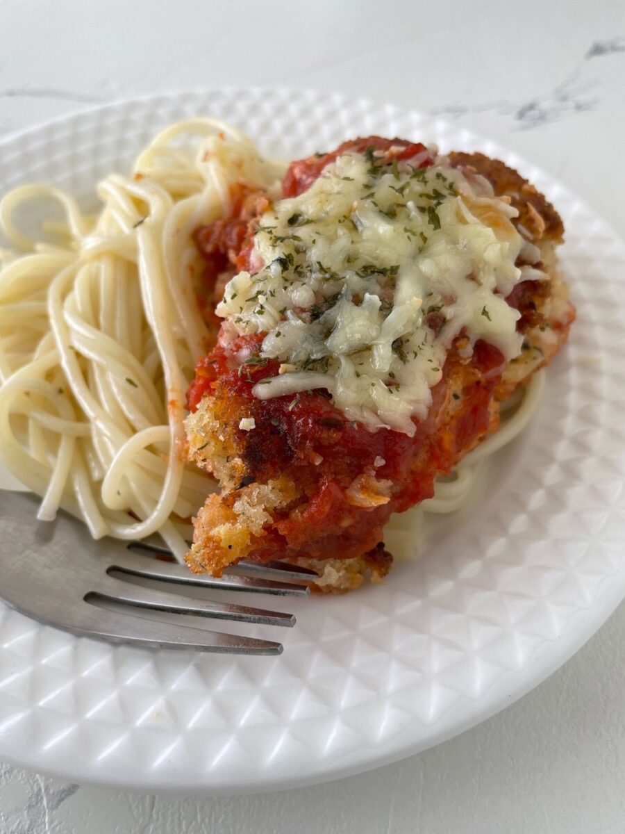 Closeup of chicken cutlet Parmesan on white plate with spaghetti.